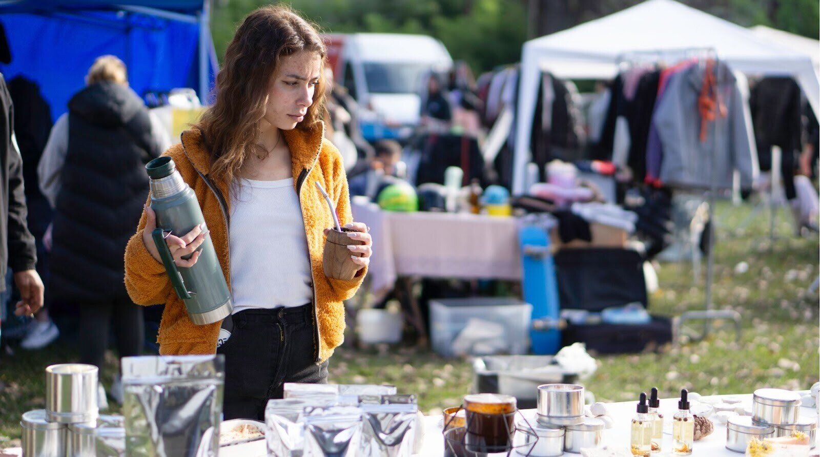 Jovem vendedor segurando garrafa térmica e erva-mate no mercado ao ar livre