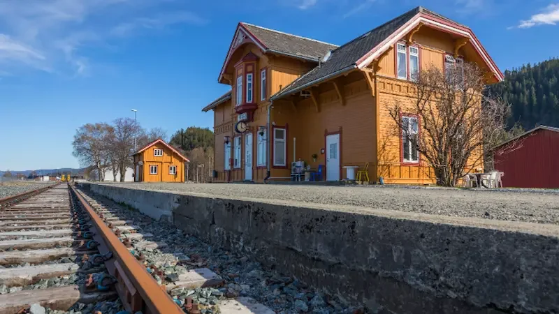 A yellow wooden stationmaster's house against a blue sky at the train station of the Norwegian village of Hell. 