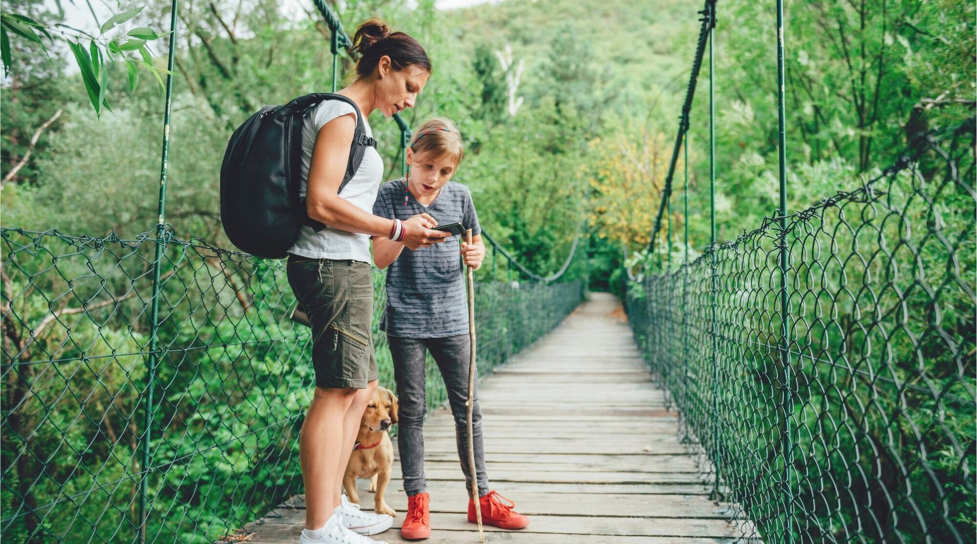 Mãe e filha em uma trilha consultando o celular.