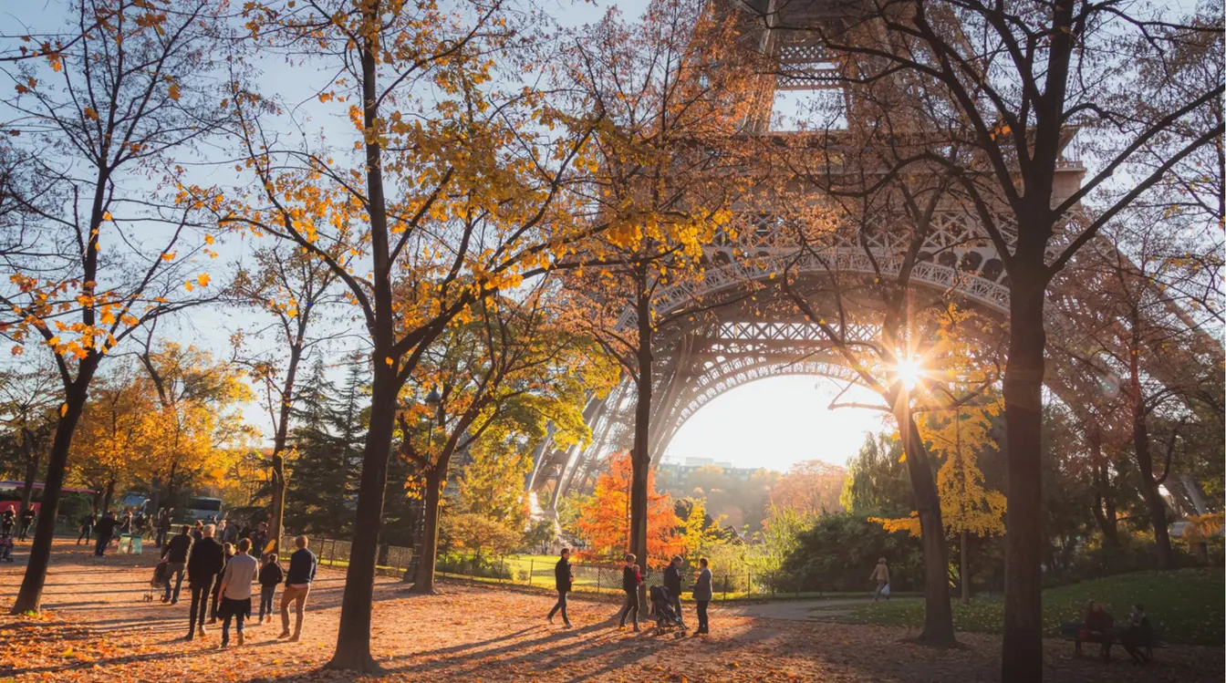 Viajantes e parisienses caminham próximos à Torre Eiffel numa manhã de outono.