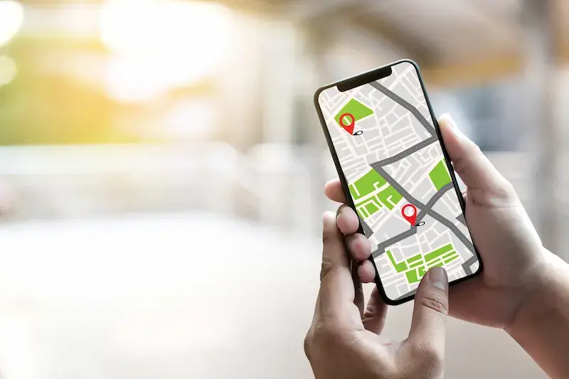 Main tenant un smartphone affichant une application de géolocalisation avec repères sur une carte
