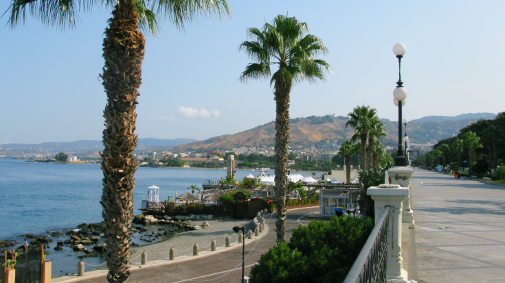 An image showing palm trees lining the Lungomare Falcomatà promenade in Reggio Calabria, overlooking the sea toward the Sicilian coast.