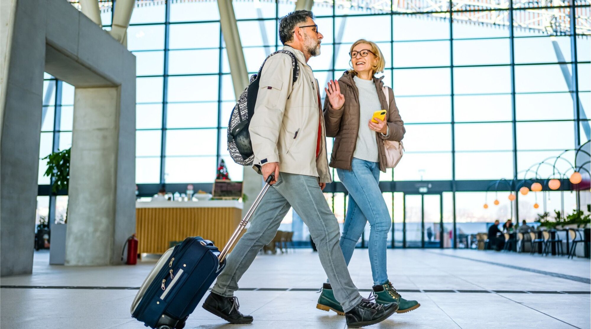 Casal viajando com bagagem de mão e mochila, caminhando pelo aeroporto