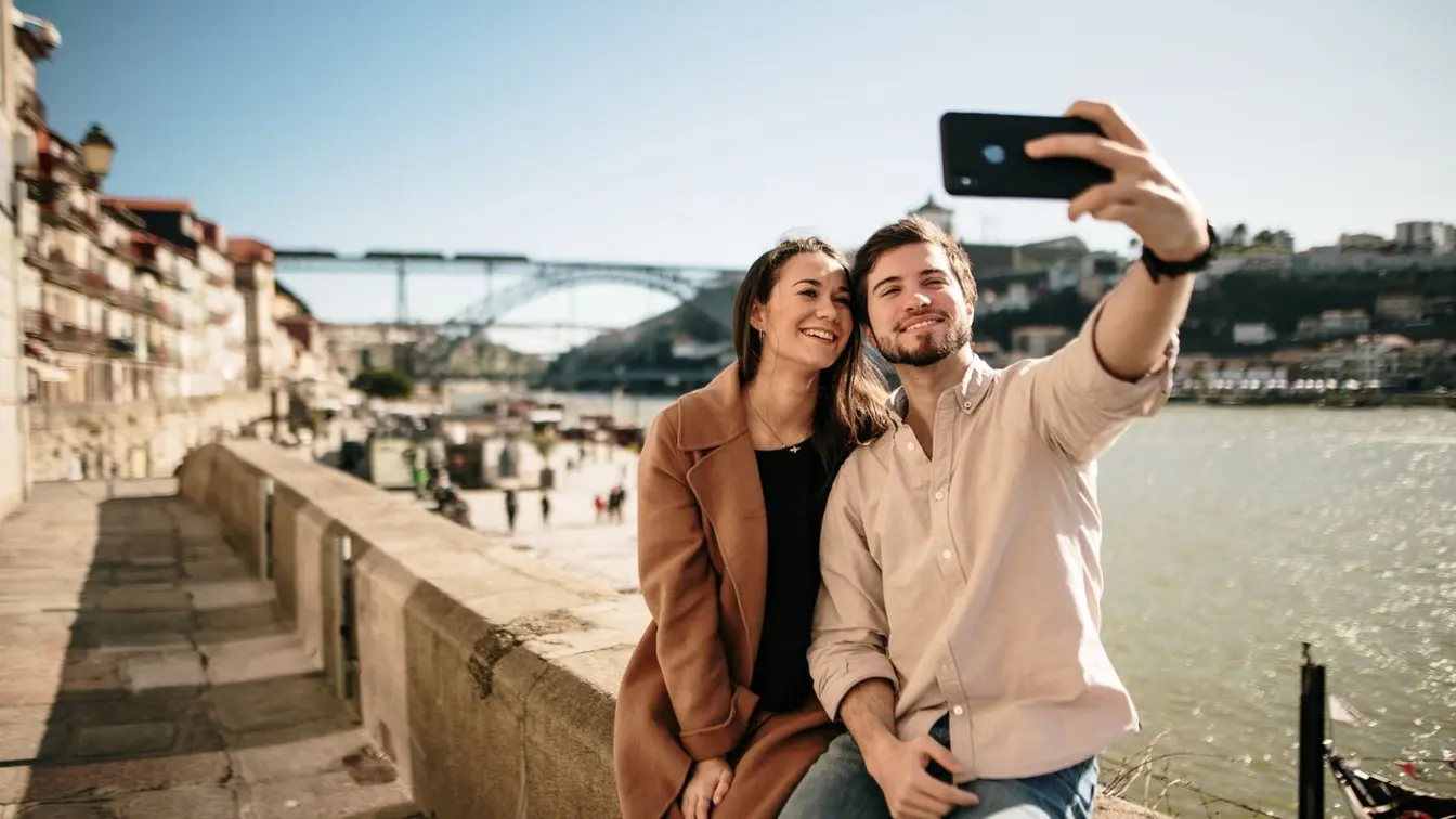 Ein Paar sitzt bei einem romantischen Urlaub am Wasser und macht ein Selfie
