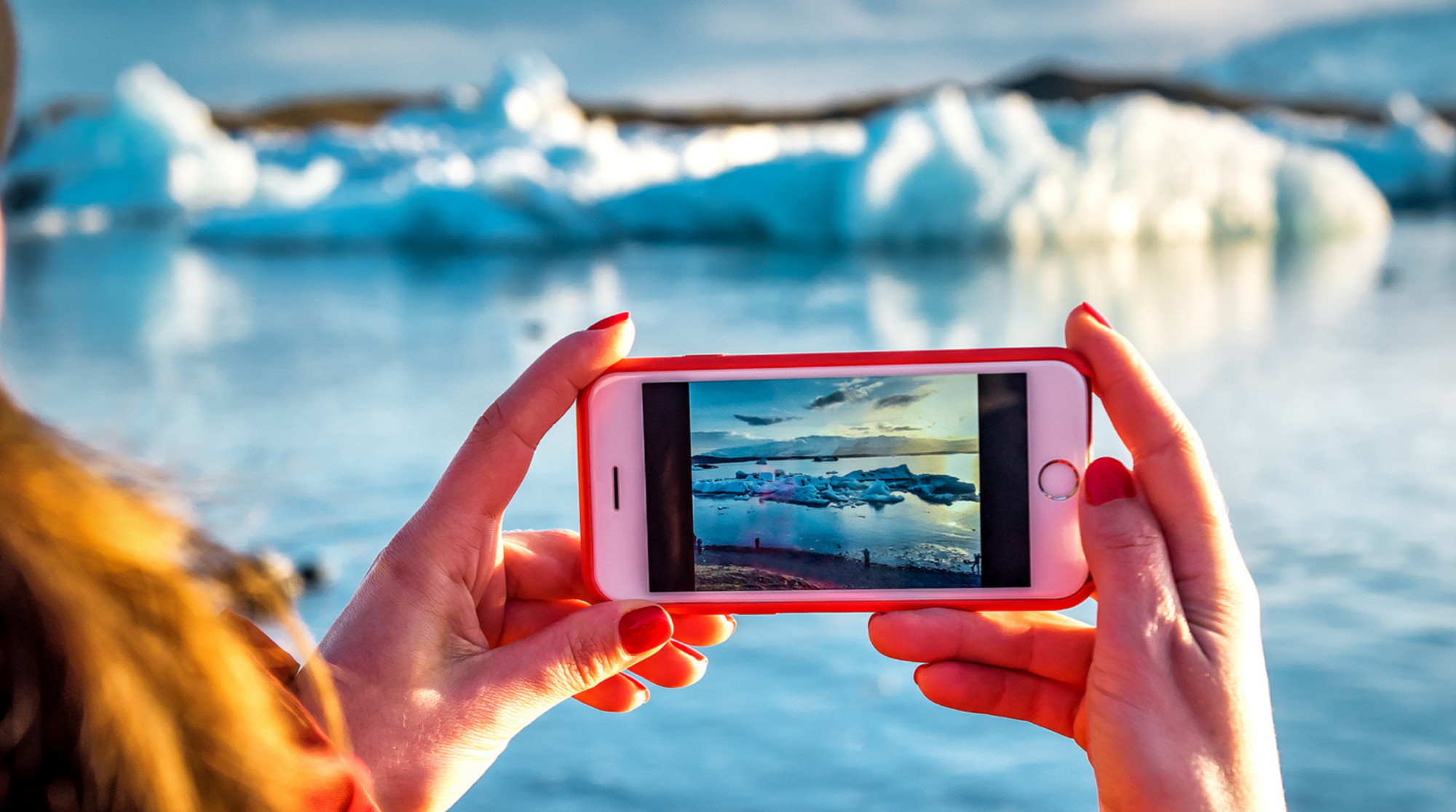 Donna che fotografa un iceberg blu nella laguna glaciale islandese usando lo smartphone durante il viaggio
