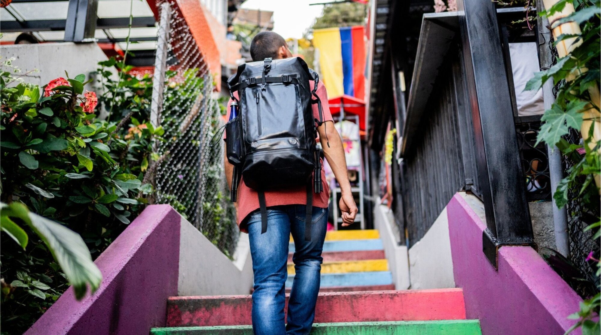 Hombre subiendo una escalera al aire libre en Medellín, con vista urbana y casas al fondo.