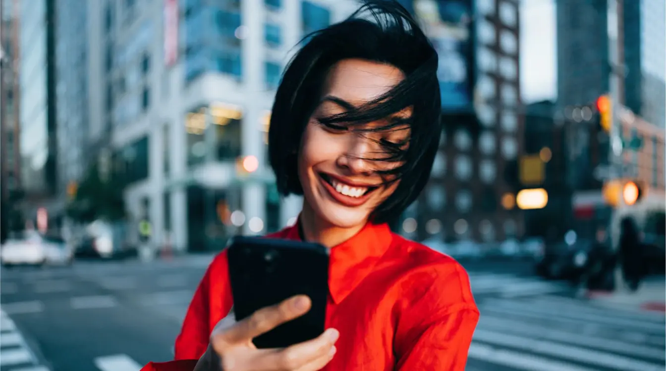 Mulher sorridente usando smartphone ao ar livre na cena de rua urbana em Nova York.
