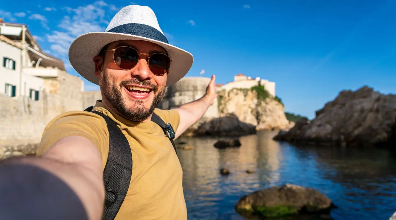 Turista che si scatta un selfie con lo smartphone davanti a una città storica europea durante un viaggio all’estero