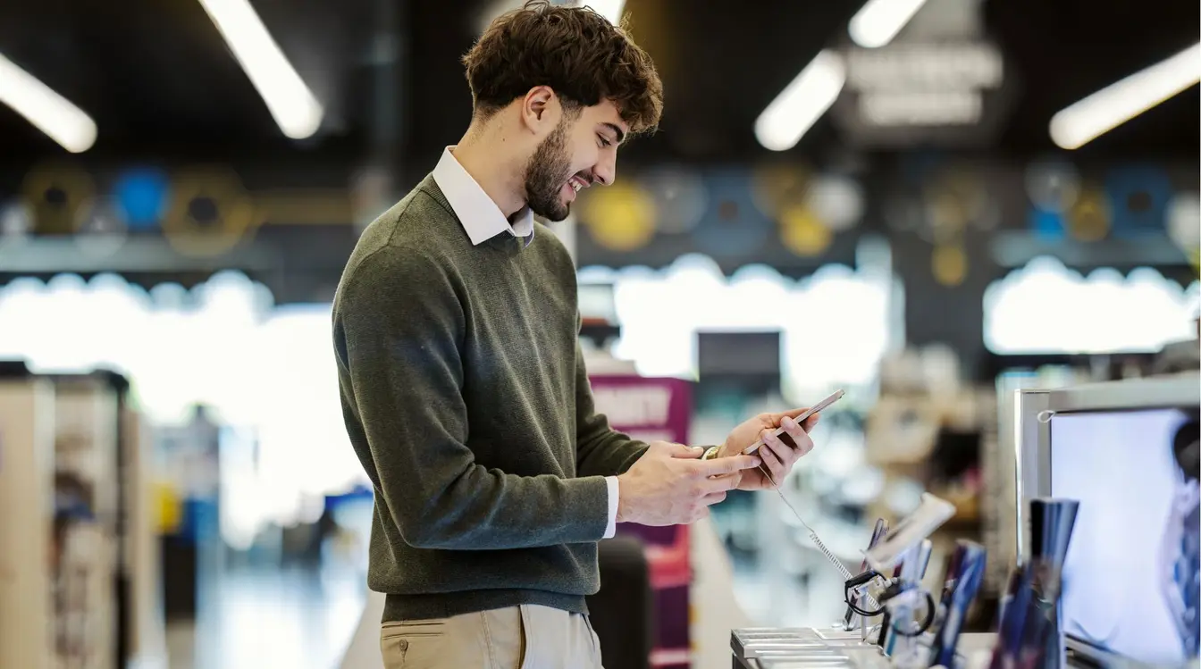 Jovem adulto comprando um smartphone novo em loja de eletrônicos.