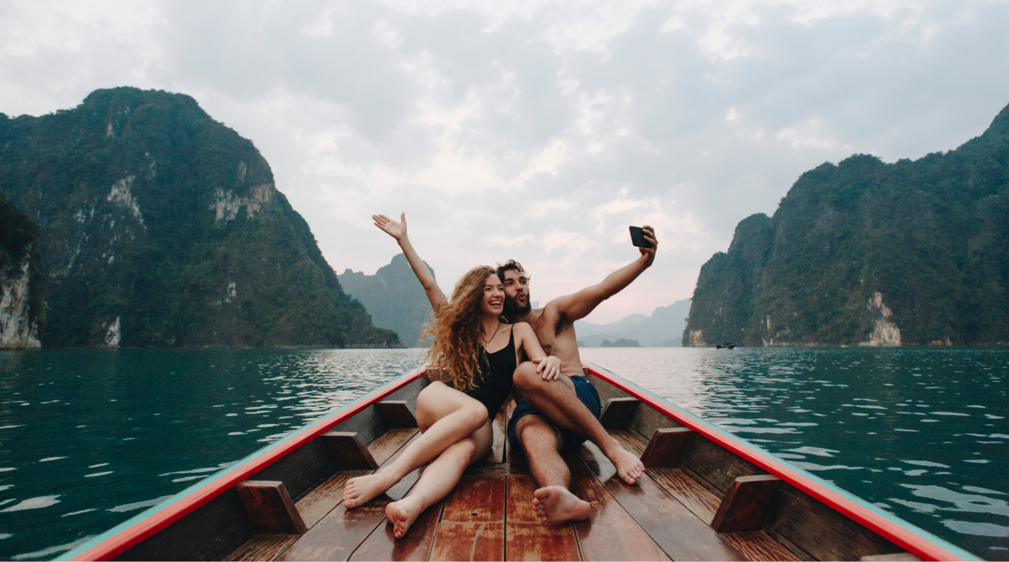 Coppia di turisti scatta un selfie su una barca longtail in Thailandia usando lo smartphone per condividere il viaggio online