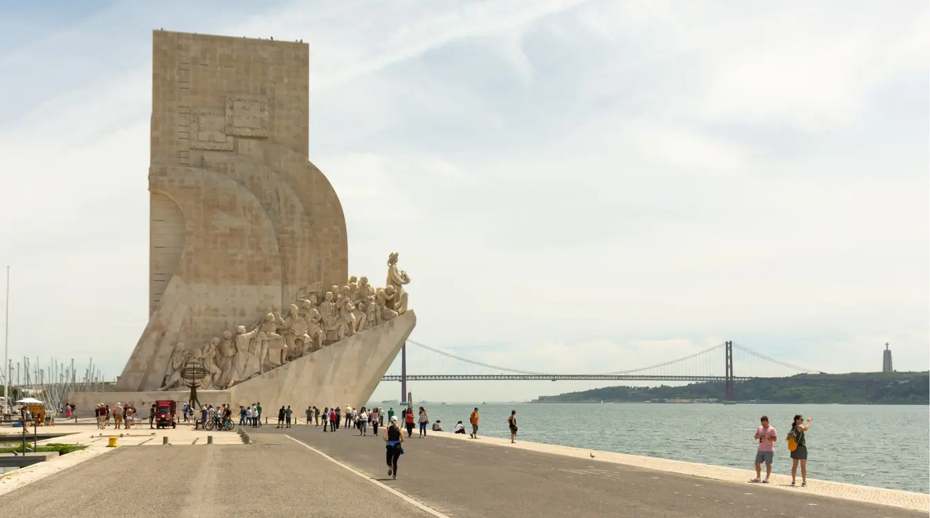 Turistas e moradores de Lisboa caminhando, andando de bicicleta, e passeando pelas margens do rio Tejo, ao lado do Padrão dos Descobrimentos, uma das principais atividades entre o que fazer em Lisboa. 
