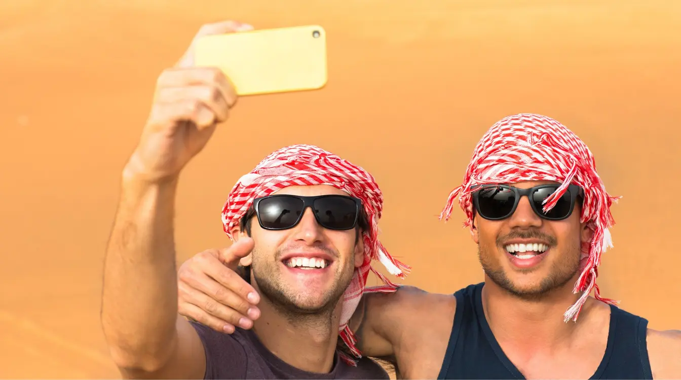 Gruppo di amici che si scatta un selfie tra le dune del deserto in Oman durante un viaggio, utilizzando lo smartphone.