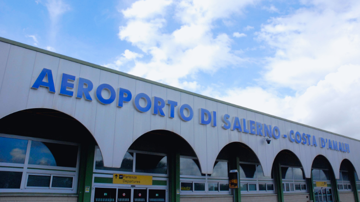 An image of the Salerno Costa d'Amalfi Airport, showing the grey archways of the terminal building against a blue sky.