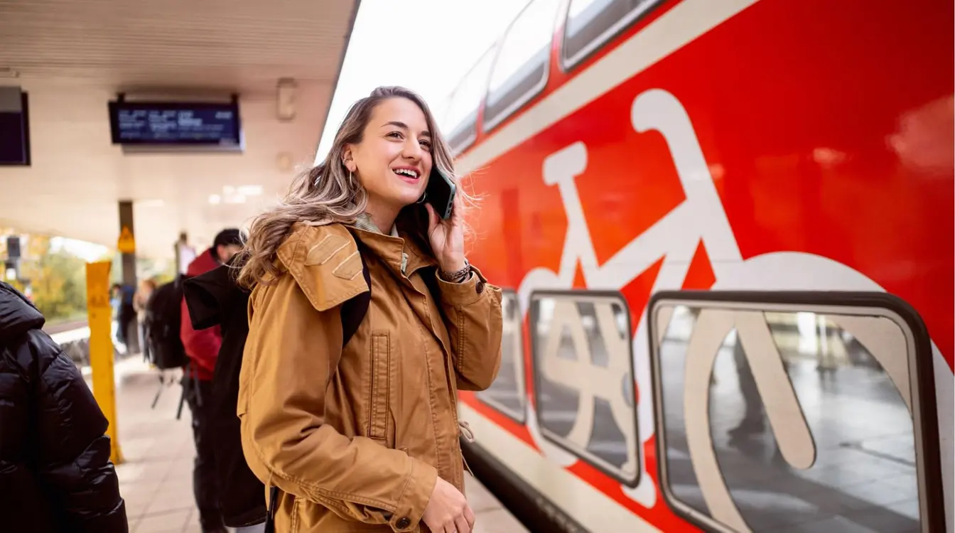Jovem mulher com roupas quentes na estação de metrô de Berlim conversando no smartphone com um trem vermelho à sua frente.