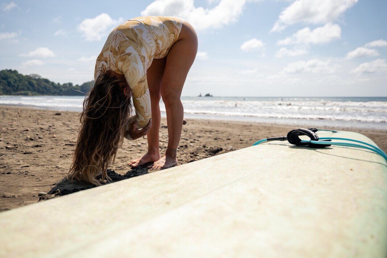 Woman stretching next to a surfboard