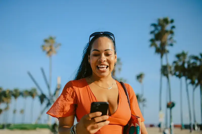 Mujer revisando su celular al aire libre en California antes de desplazarse por la ciudad.