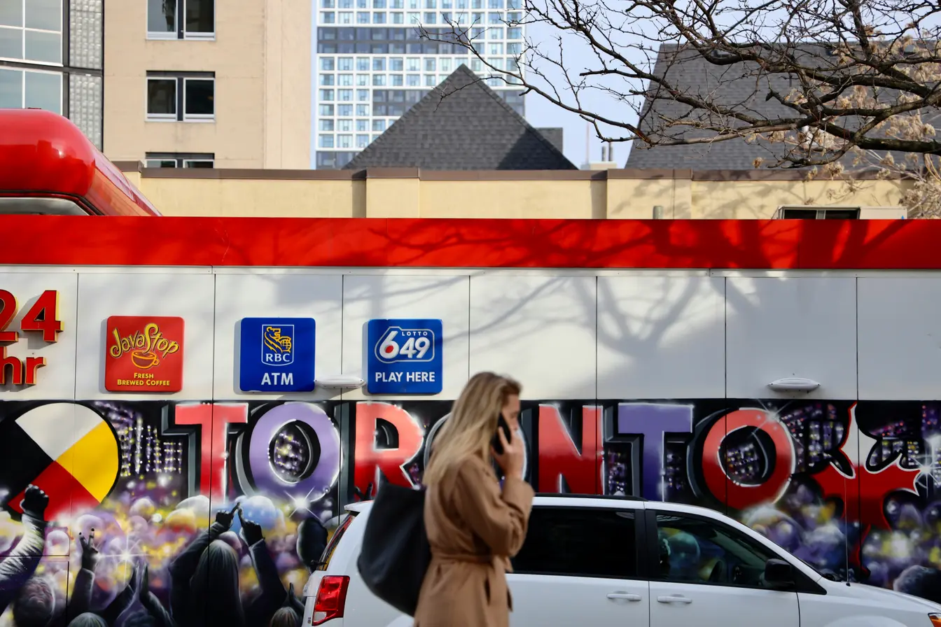Una persona hablando por teléfono camina frente a una pared decorada con un grafiti con la palabra “Toronto” para ilustrar la conexión en tu viaje a Toronto.
