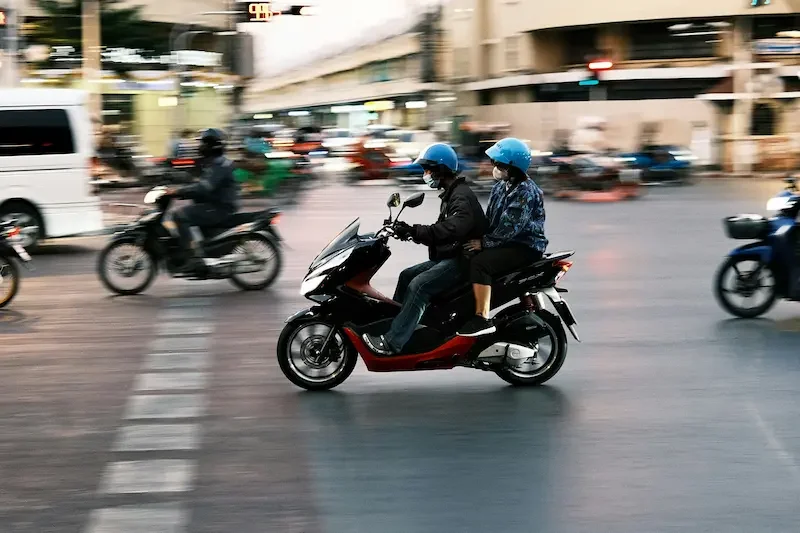 Two people riding a motorbike through busy city traffic in Bangkok, Thailand.
