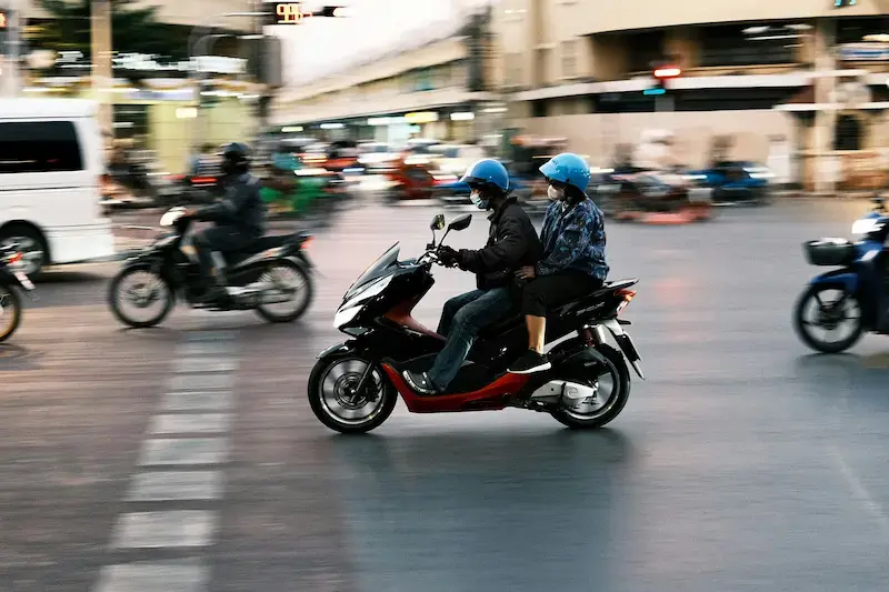 Two people riding a motorbike through busy city traffic in Bangkok, Thailand.