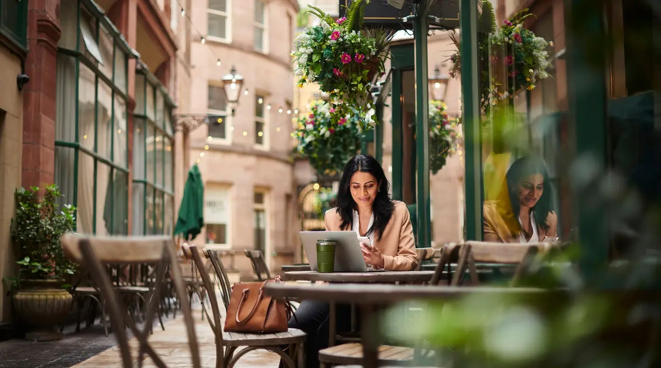 En ung kvinne sitter foran en kafé og ser på smarttelefonen sin.
