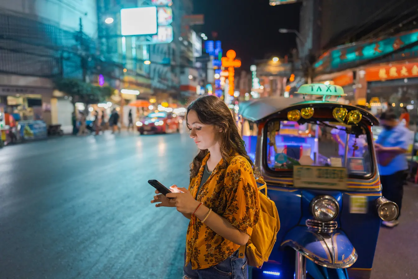 Woman on her phone near a tuk-tuk in Bangkok.
