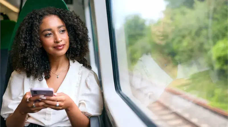 Mujer viajando en tren mientras revisa su teléfono móvil durante un trayecto