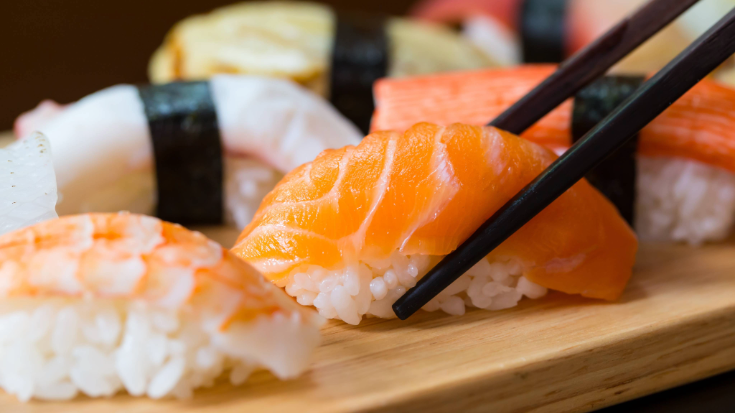 Close-up of colourful sushi on a wooden platter, with chopsticks lifting fresh salmon nigiri, a must-try Japanese food experience for Tokyo Game Show visitors exploring Tokyo.