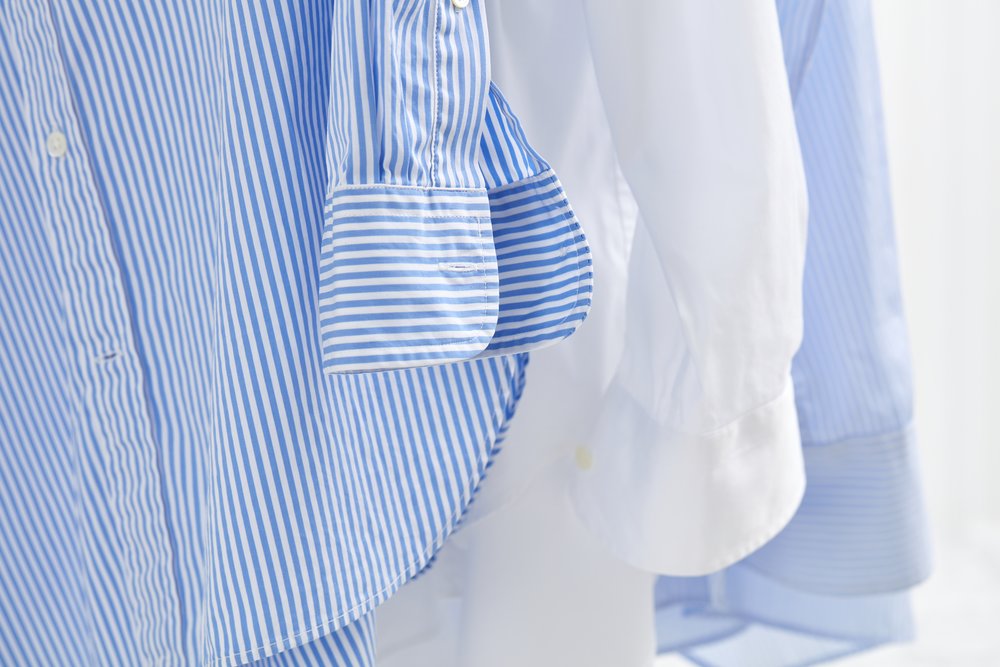 Three blue and white button-down collared shirts hanging up to be steamed.
