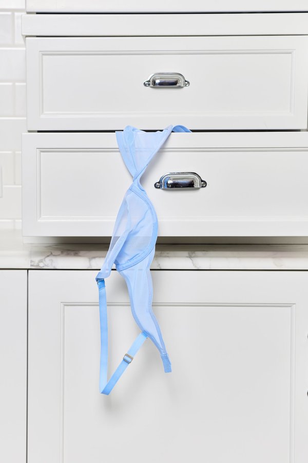 A blue bra hanging out of a white dresser drawer.