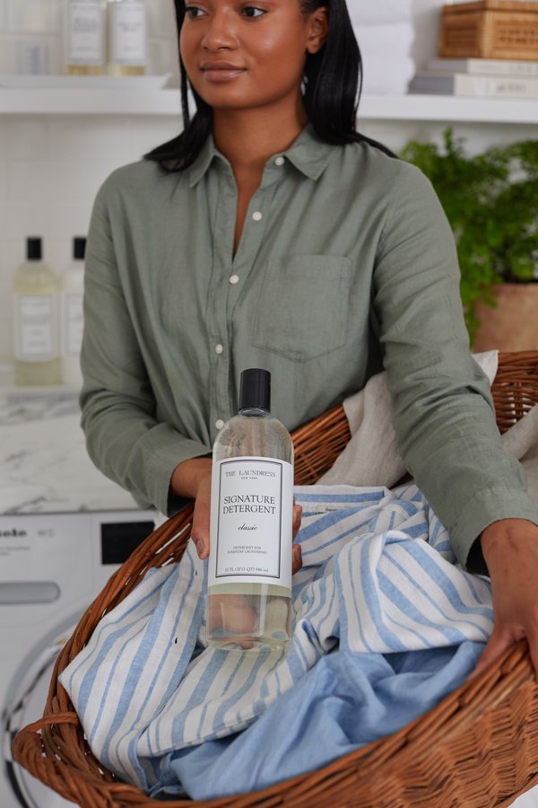 Woman holding The Laundress Signature Detergent in laundry room