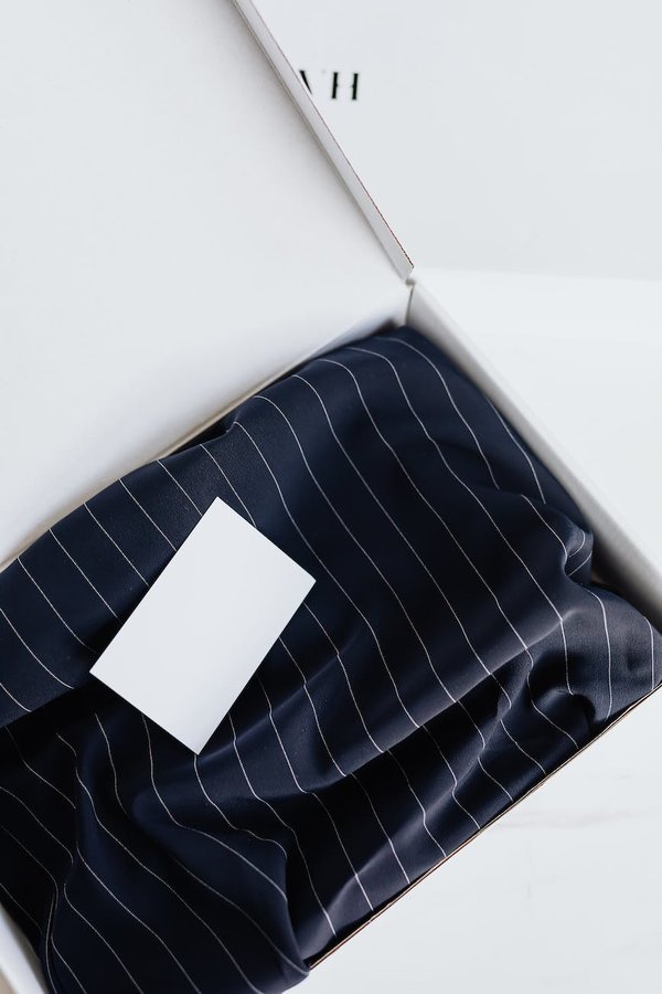 A white box with a navy and white pinstriped clothing item and a white notecard inside. 