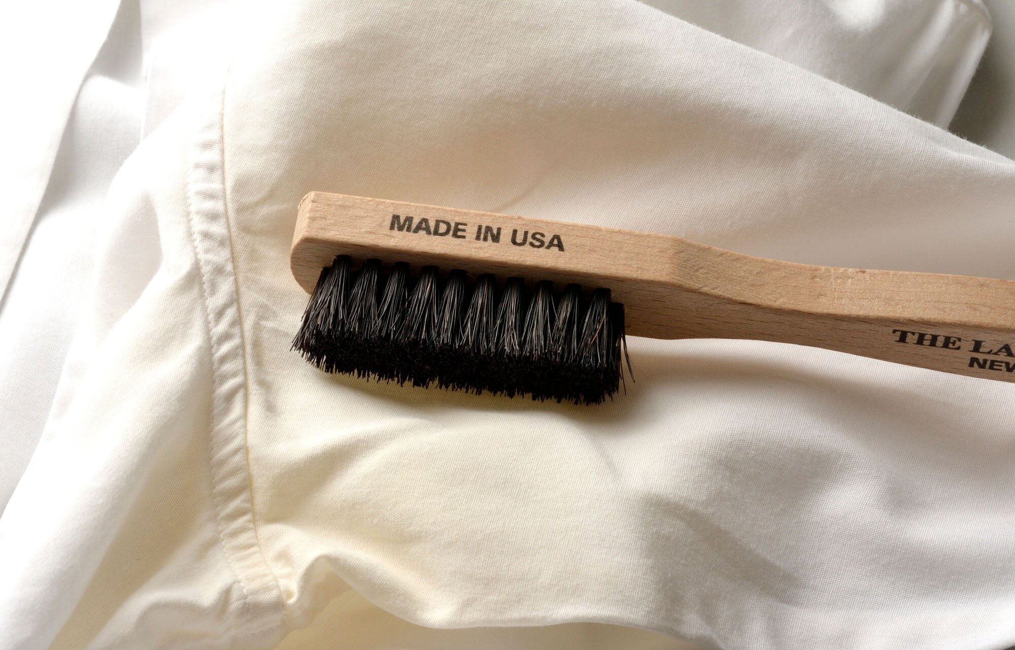 The Laundress Stain Brush, ideal for removing stains on washable fabrics, rests on white fabric.