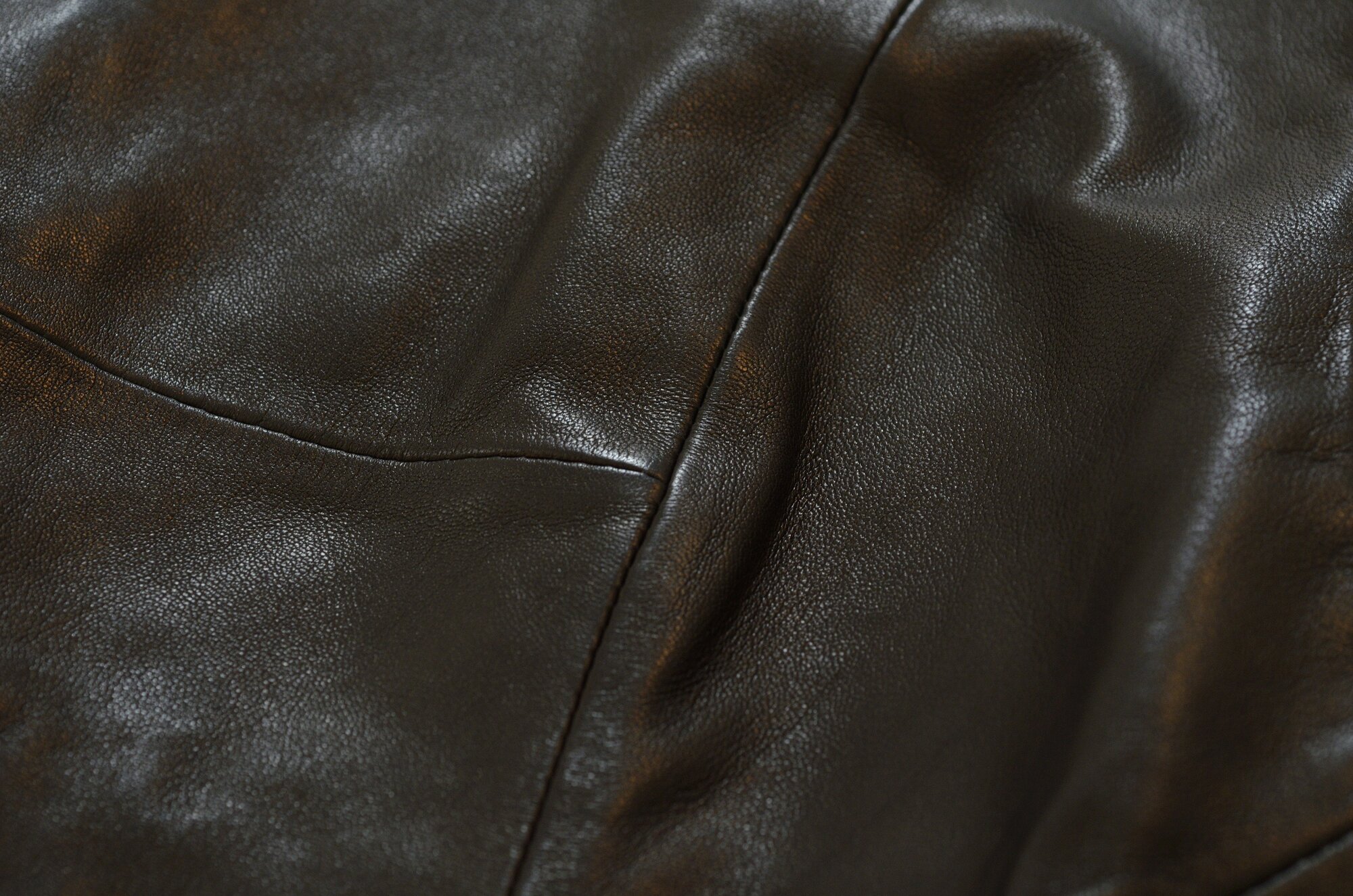 Dark brown leather close-up, featuring detailed texture and stitching lines, under soft lighting, which has been cleaned using The Laundress' dry cleaning method.
