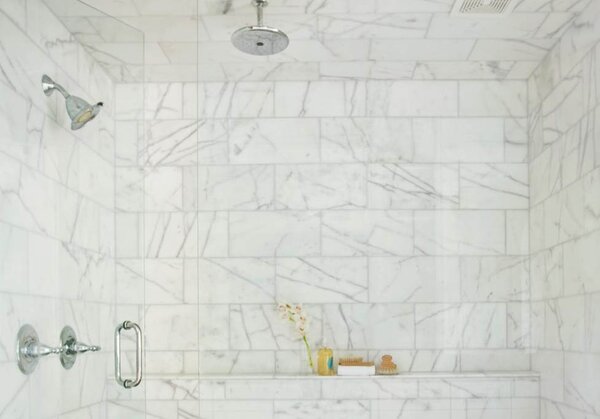 A bathroom shower with white marble tiles, cleaned using The Laundress's expert tile and grout cleaning method.