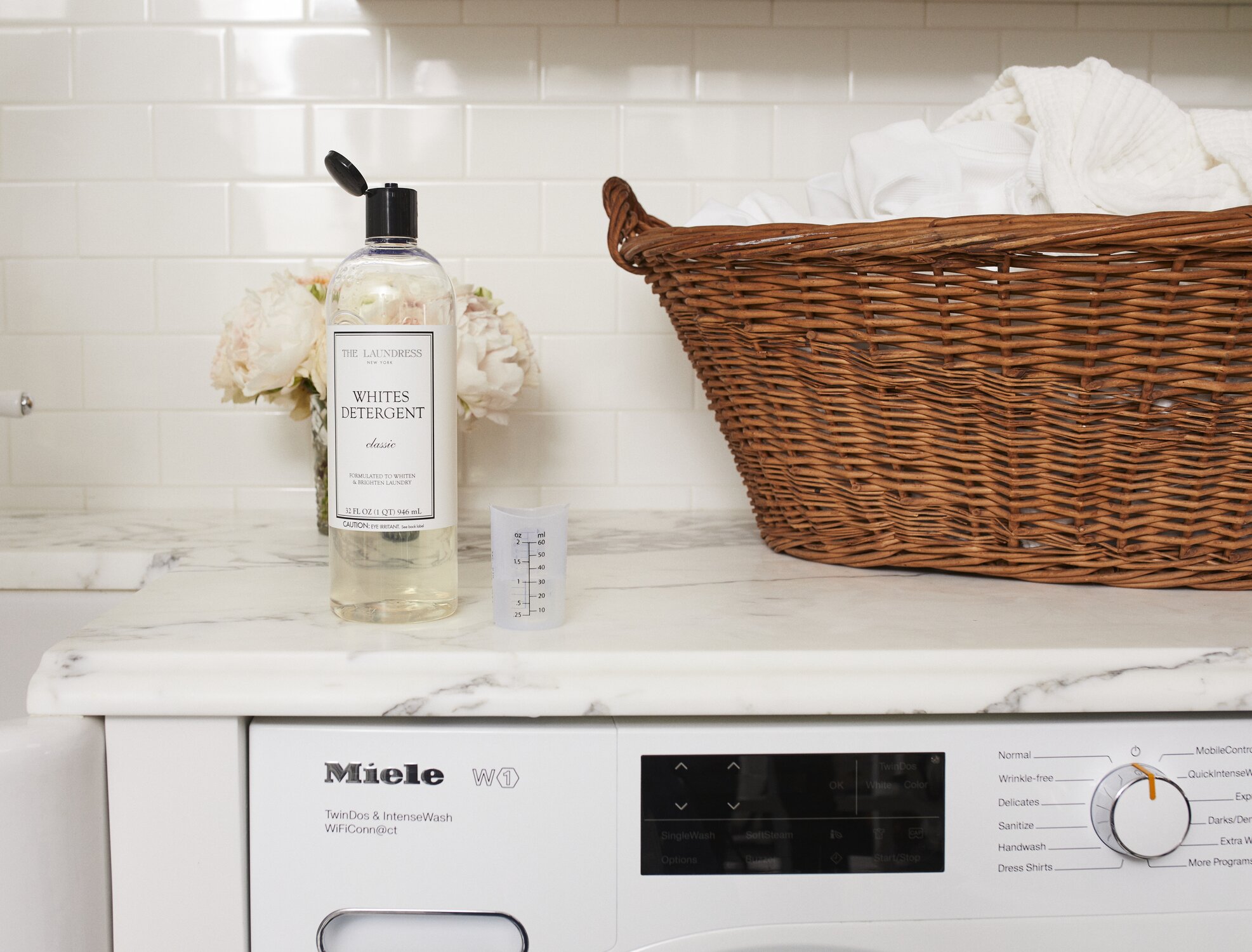 the laundress whites detergent and measuring cup on a counter next to a basket of white laundry