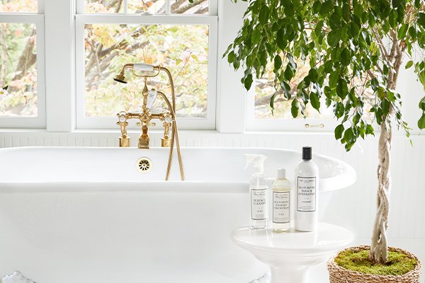 The Laundress Surface Cleaner, All-Purpose Cleaning Concentrate and All-Purpose Bleach Alternative in bathroom next to tub