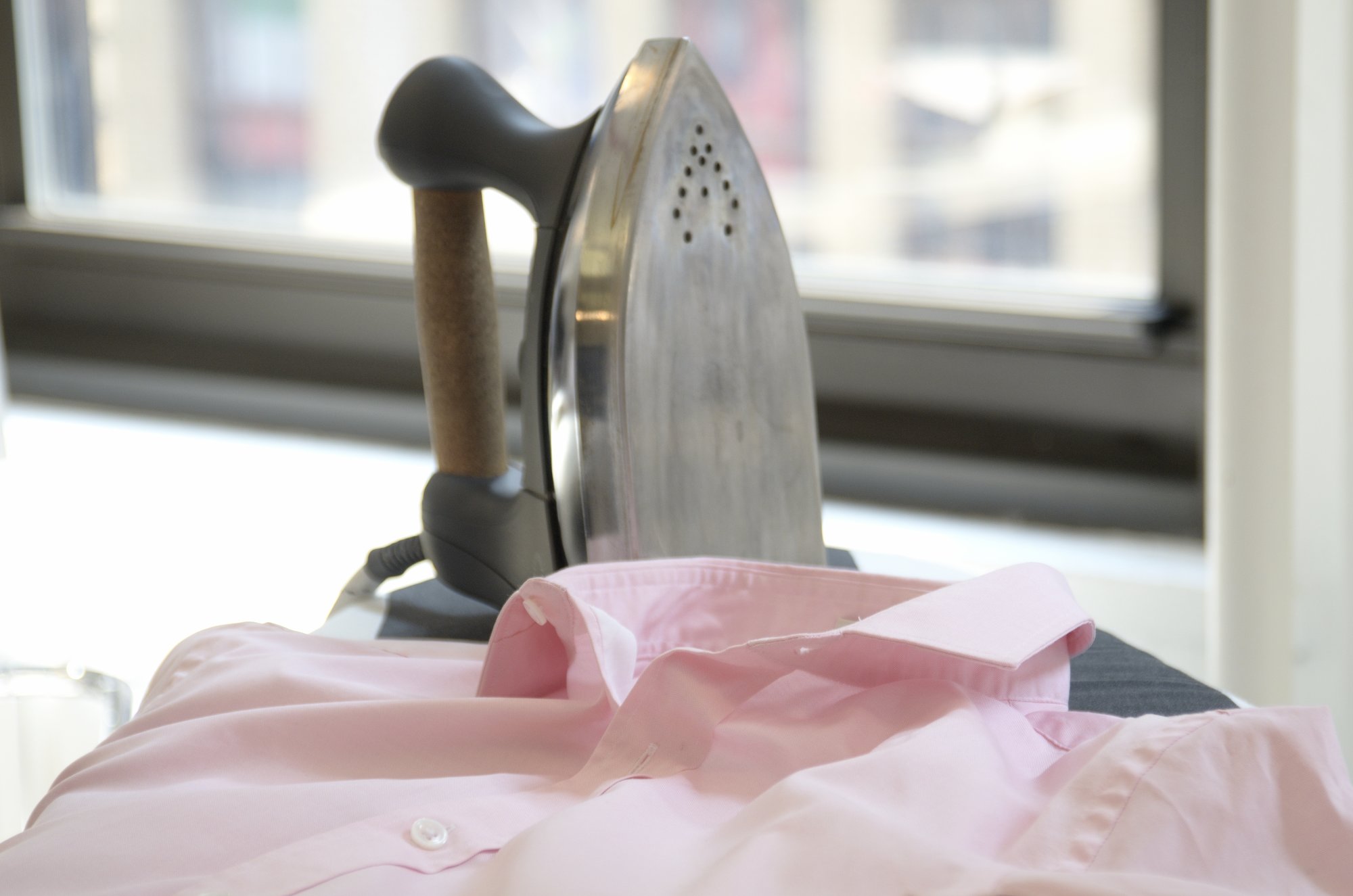 Iron on ironing board with pink button down shirt.
