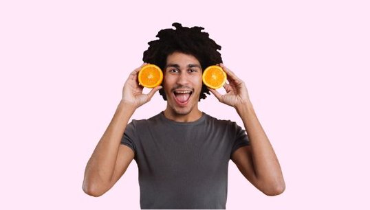 man holding 2 oranges with pink background