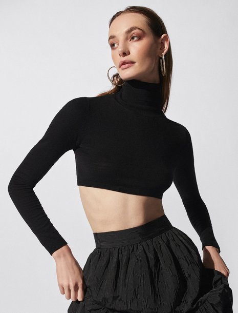 Woman wearing a cropped black turtleneck with a high-waisted black skirt