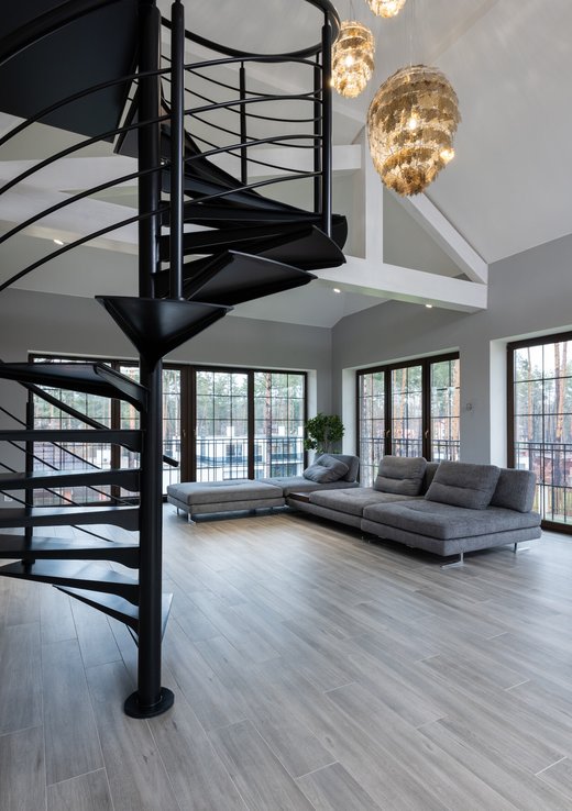 spacious room with wide windows, a gray sofa, chandelier, and spiral staircase