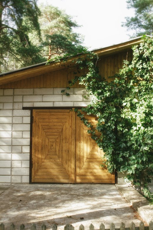 a garage made of white bricks with closed wooden doors surrounded by trees