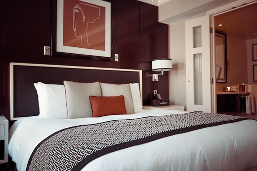 a king-size hotel bed in a wooden-style bedroom. The wall showcases an elegant portrait, and the bed is adorned with stylish bedding.