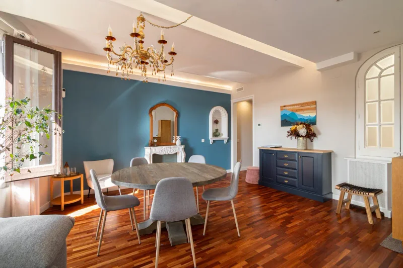 Comedor luminoso con pared azul, mesa redonda y lámpara de araña