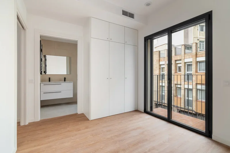 Dormitorio con armario blanco, balcón y baño