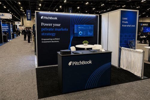PitchBook financial software booth with professional navy and white branding, large backlit display stating 'Power your private markets strategy,' branded reception counter, minimal seating area, and clean geometric line accents