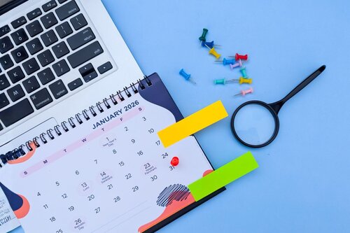 Overhead view of organized desk workspace with January 2026 calendar, laptop, colorful push pins, sticky notes, and magnifying glass for post-show follow-up