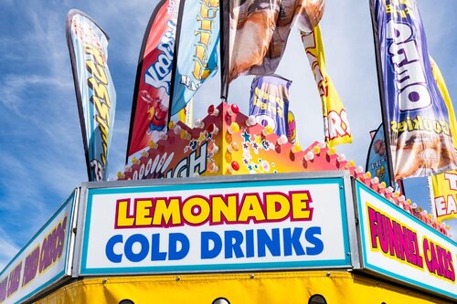 Lemonade stand at carnival surrounded by towering feather flags in front of the sky