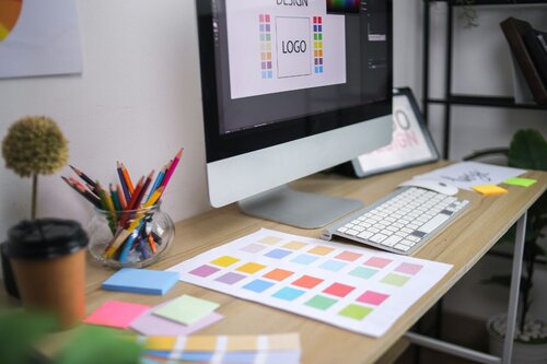 Graphic designing on a computer with pantones scattered on the table.