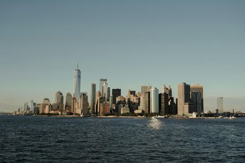 Manhattan from the view across water. The sky is clear and blue and the water is dark blue.