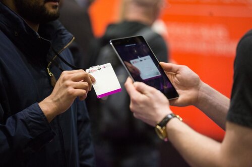 A person scanning an event badge with a smartphone at a trade show or conference.